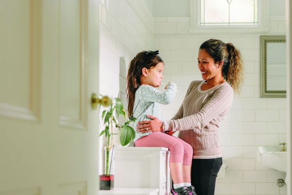 Mother helping daughter brush teeth in bathroom